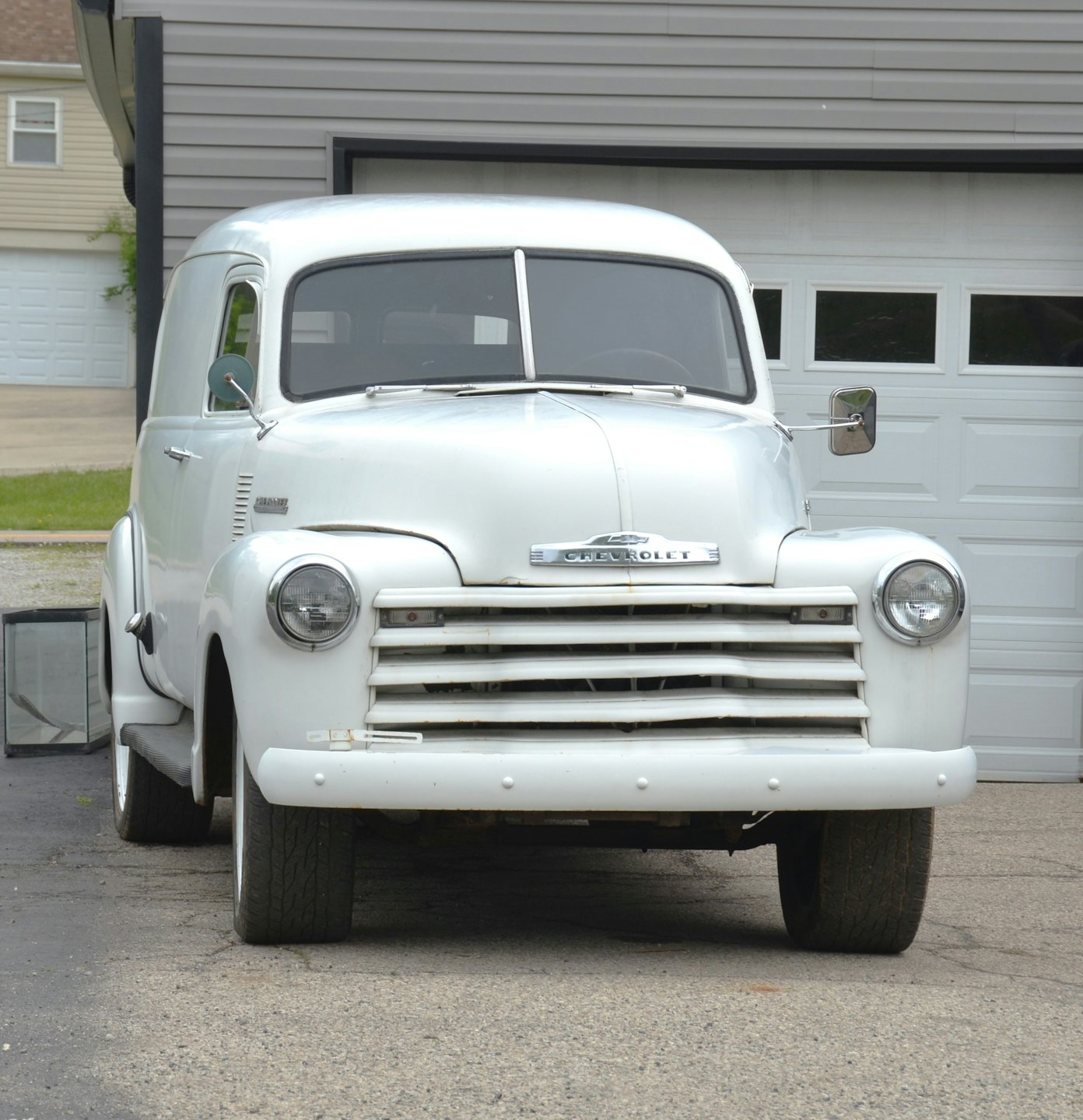 A white vintage Chevrolet van parked on a suburban driveway.