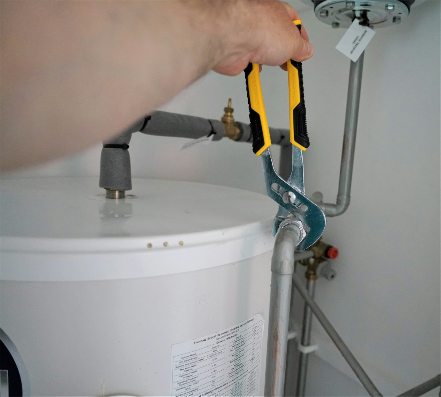 Hand using pliers to turn a fitting on a water heater pipe.